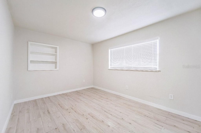 unfurnished room featuring built in shelves and light hardwood / wood-style flooring