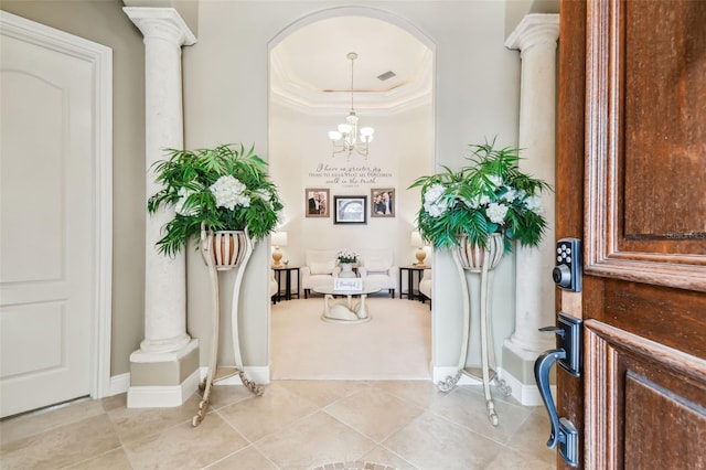 entryway featuring an inviting chandelier, crown molding, ornate columns, light tile patterned floors, and a tray ceiling