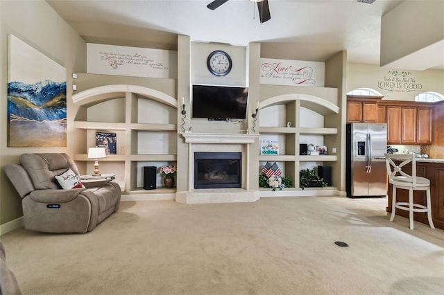 carpeted living area with built in shelves, a glass covered fireplace, visible vents, and a ceiling fan