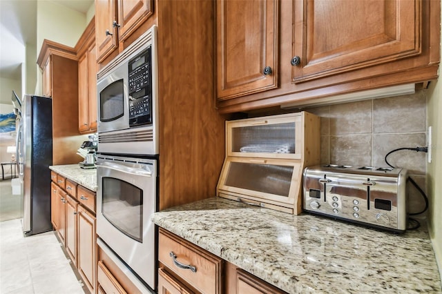 kitchen with a toaster, decorative backsplash, appliances with stainless steel finishes, brown cabinetry, and light stone countertops