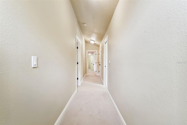 hall featuring a textured ceiling, light carpet, and lofted ceiling