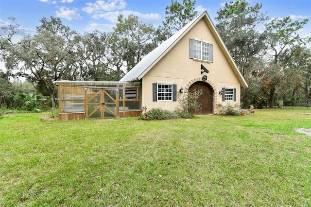 tudor-style house with stucco siding, a front lawn, metal roof, and an outdoor structure