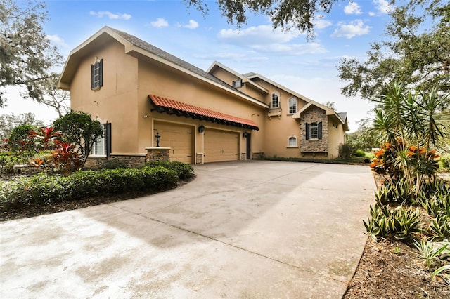 view of front of property featuring an attached garage, stone siding, concrete driveway, and stucco siding