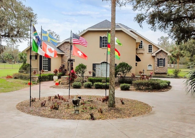 view of front of house featuring stone siding, curved driveway, and stucco siding