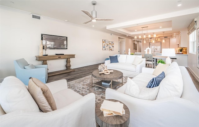 living room featuring a tray ceiling, dark wood-type flooring, and ceiling fan with notable chandelier