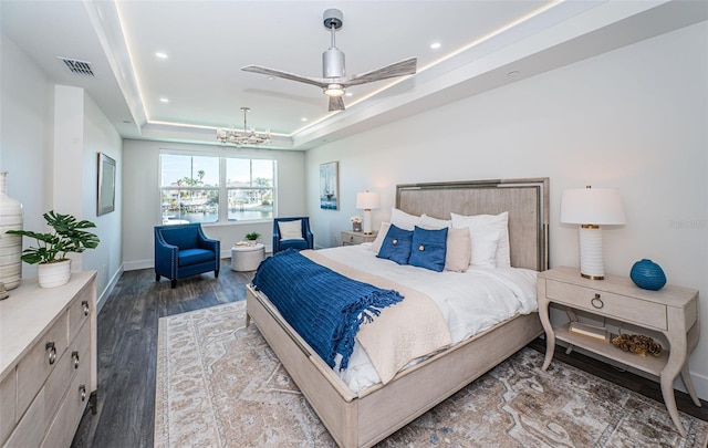 bedroom featuring a raised ceiling, dark wood-type flooring, and ceiling fan with notable chandelier