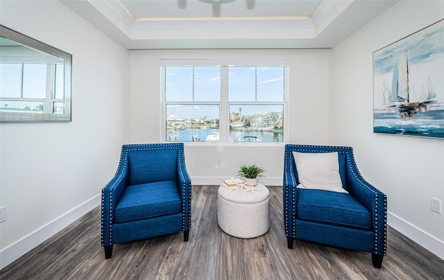 living area with a water view, crown molding, a tray ceiling, and dark wood-type flooring