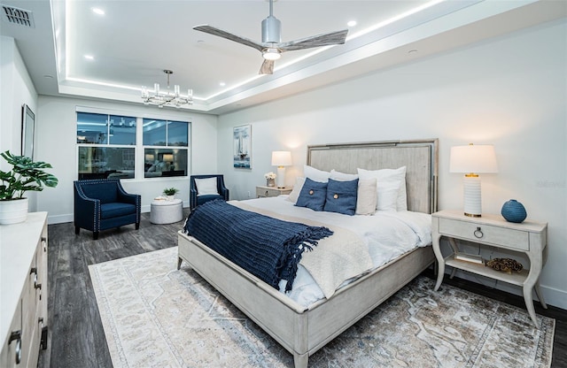 bedroom with ceiling fan with notable chandelier, dark hardwood / wood-style flooring, and a raised ceiling