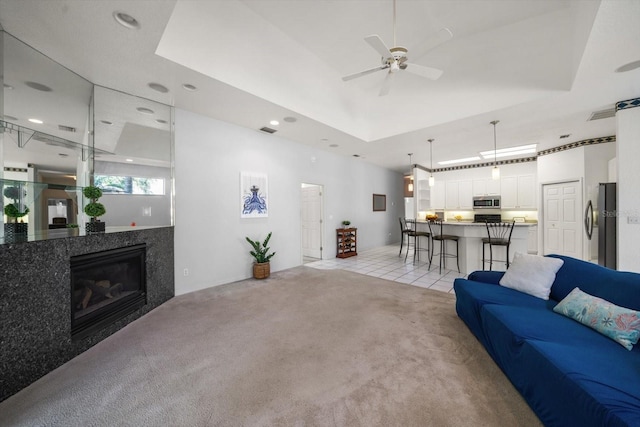 living room featuring a raised ceiling, ceiling fan, and light colored carpet