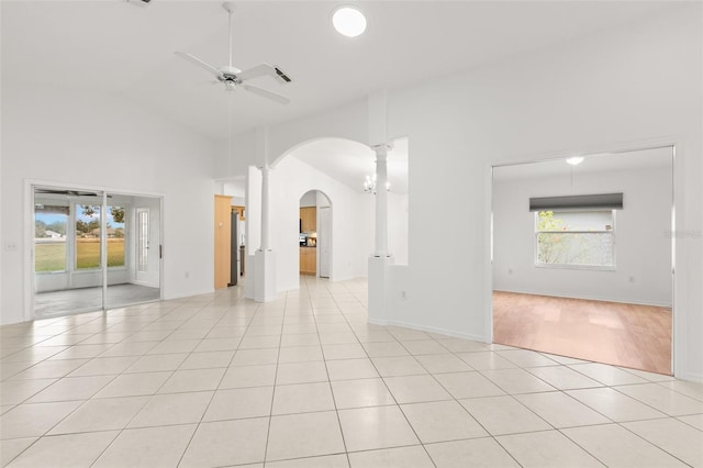 unfurnished room with light tile patterned floors, ceiling fan with notable chandelier, high vaulted ceiling, and ornate columns