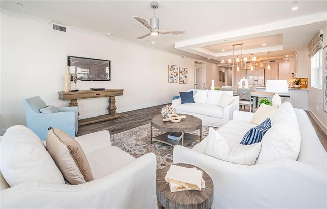 living room featuring ceiling fan with notable chandelier, dark hardwood / wood-style flooring, and a tray ceiling