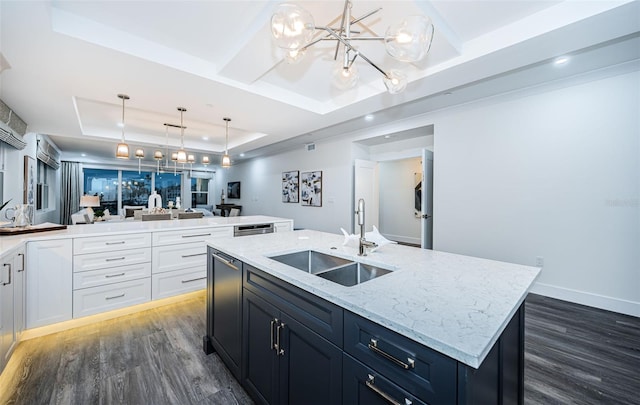 kitchen with a raised ceiling, dark wood-type flooring, sink, a center island with sink, and decorative light fixtures