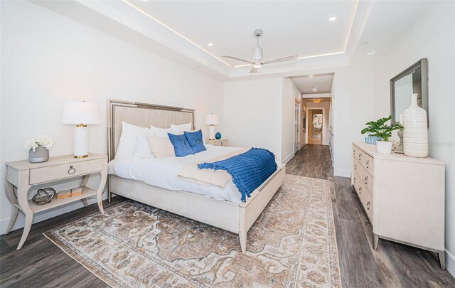 bedroom featuring a raised ceiling, ceiling fan, and dark hardwood / wood-style flooring