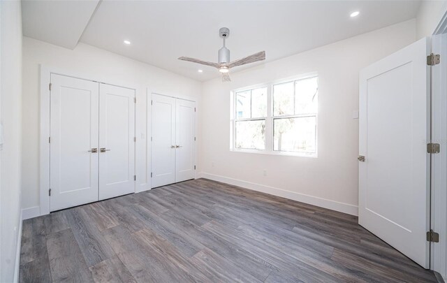 unfurnished bedroom featuring ceiling fan, dark hardwood / wood-style floors, and two closets