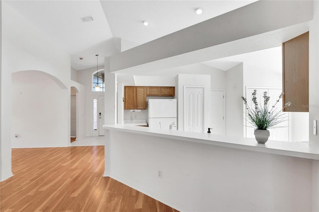 kitchen featuring kitchen peninsula, light hardwood / wood-style floors, vaulted ceiling, and white refrigerator