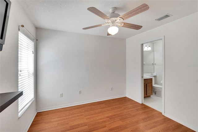 unfurnished bedroom featuring a textured ceiling, connected bathroom, light hardwood / wood-style floors, and ceiling fan