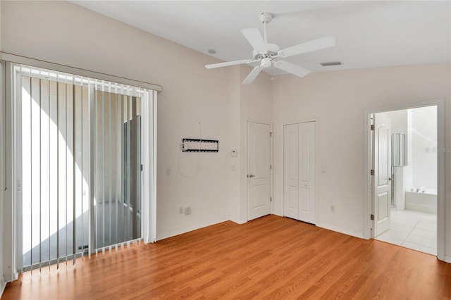 unfurnished bedroom featuring ensuite bathroom, vaulted ceiling, ceiling fan, light wood-type flooring, and multiple closets