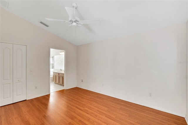 unfurnished bedroom featuring lofted ceiling, ceiling fan, connected bathroom, light hardwood / wood-style floors, and a closet