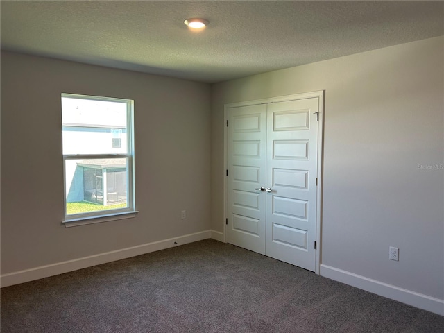 unfurnished bedroom with a closet, dark carpet, and a textured ceiling