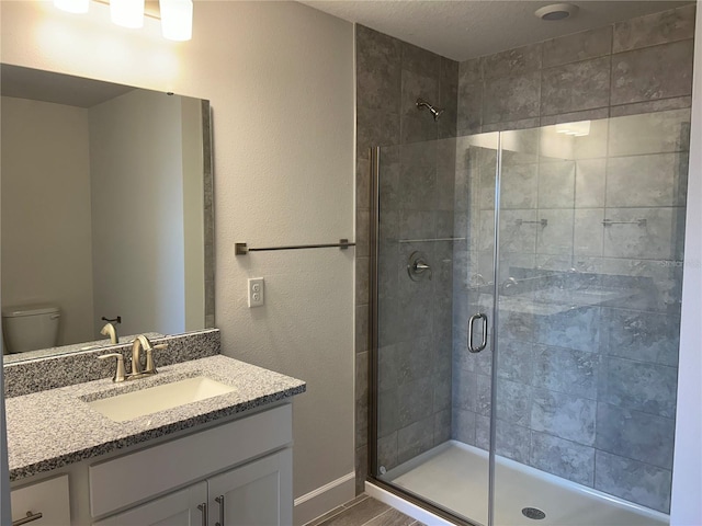 bathroom featuring a shower with door, vanity, and toilet