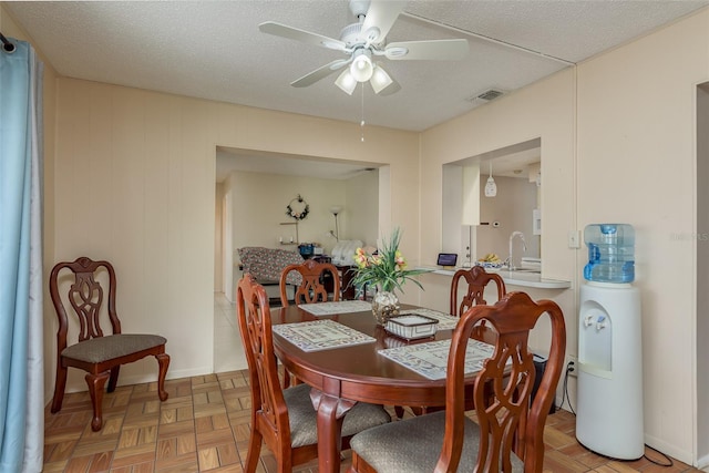 dining area with ceiling fan, sink, a textured ceiling, and light parquet flooring