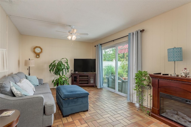 living room with ceiling fan, wooden walls, light parquet flooring, and a textured ceiling