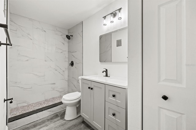 bathroom featuring a tile shower, hardwood / wood-style floors, vanity, and toilet