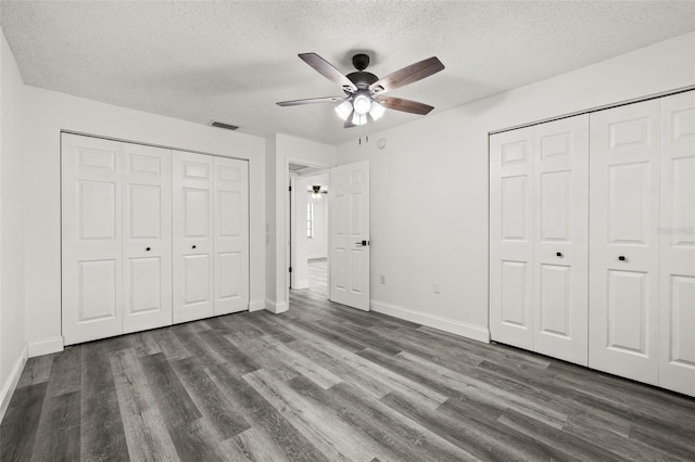 unfurnished bedroom with a textured ceiling, dark hardwood / wood-style flooring, ceiling fan, and multiple closets