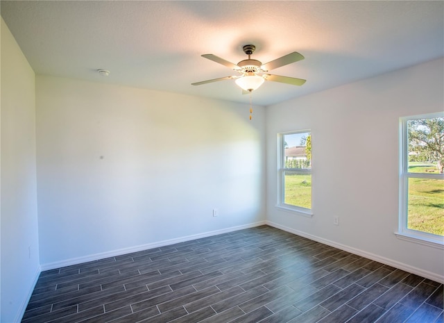 empty room with a wealth of natural light, ceiling fan, dark wood-type flooring, and a textured ceiling