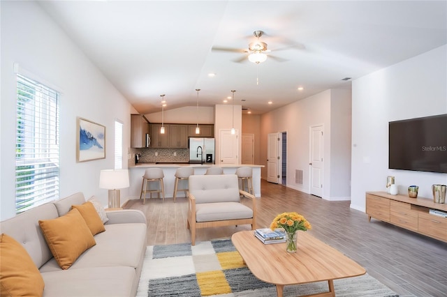 living room featuring ceiling fan, light hardwood / wood-style floors, and vaulted ceiling