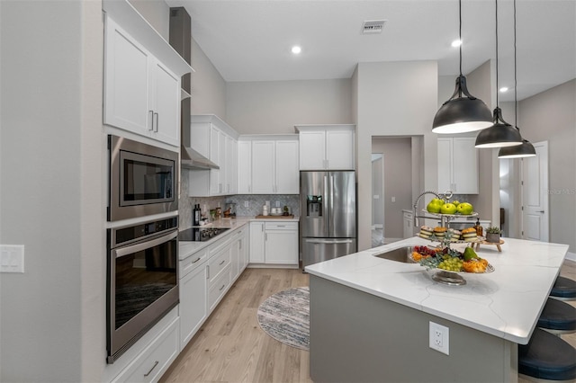 kitchen with white cabinetry, a kitchen island with sink, stainless steel appliances, and light stone counters