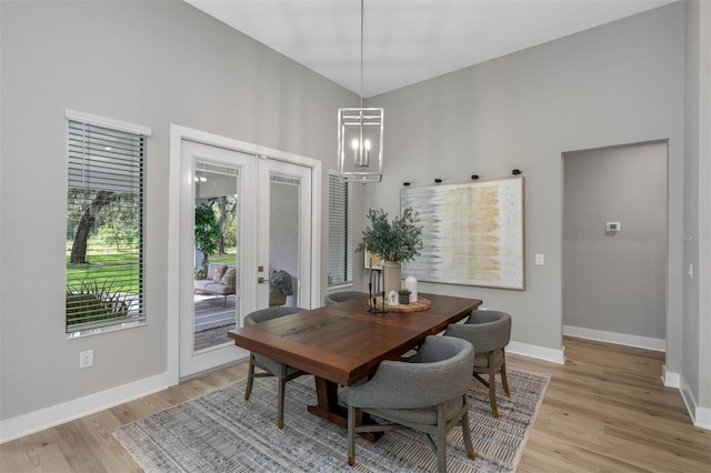 dining area with french doors, a towering ceiling, light hardwood / wood-style floors, and an inviting chandelier