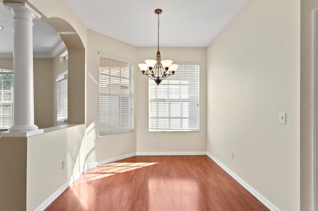 unfurnished dining area featuring wood-type flooring, an inviting chandelier, a wealth of natural light, and crown molding