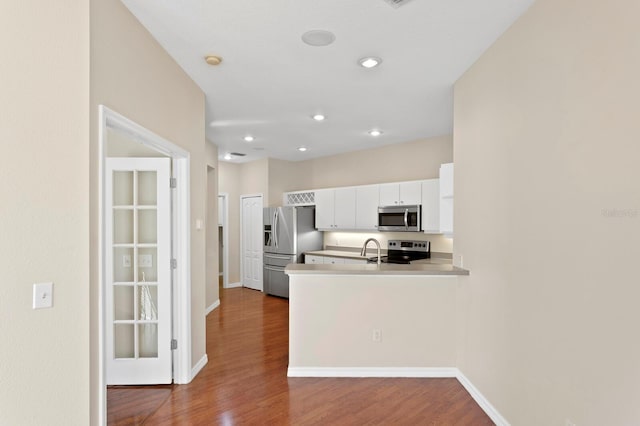 kitchen featuring kitchen peninsula, white cabinetry, hardwood / wood-style floors, and stainless steel appliances