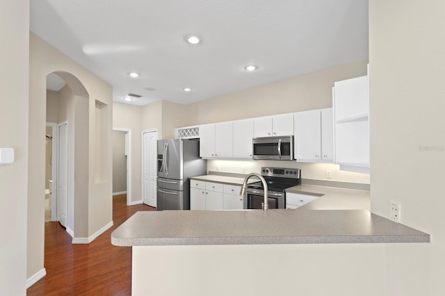 kitchen with white cabinetry, kitchen peninsula, stainless steel appliances, and dark wood-type flooring