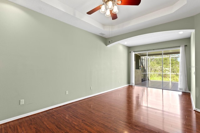 empty room featuring a raised ceiling, ceiling fan, and hardwood / wood-style floors