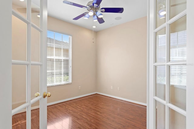 empty room featuring ceiling fan, a healthy amount of sunlight, wood-type flooring, and french doors