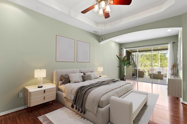 bedroom featuring ceiling fan, access to exterior, dark wood-type flooring, and a tray ceiling