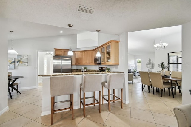 kitchen with vaulted ceiling, light tile patterned floors, light stone counters, kitchen peninsula, and stainless steel appliances