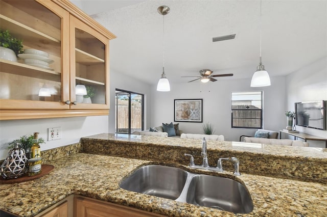 kitchen featuring ceiling fan, sink, dark stone countertops, a textured ceiling, and decorative light fixtures