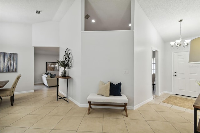 tiled foyer entrance with a textured ceiling, high vaulted ceiling, and an inviting chandelier