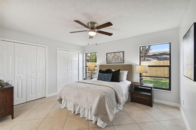 tiled bedroom with a textured ceiling, ceiling fan, and two closets