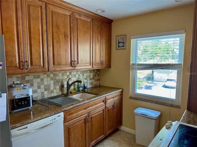 kitchen with dishwasher, dark stone counters, sink, decorative backsplash, and light tile patterned floors