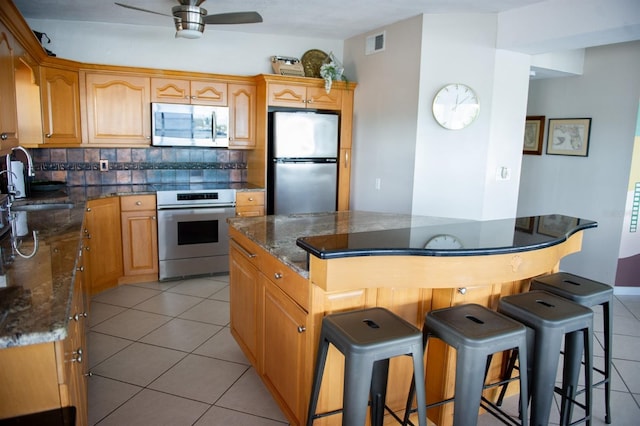 kitchen featuring backsplash, ceiling fan, dark stone countertops, light tile patterned floors, and stainless steel appliances