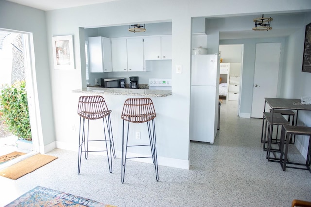 kitchen with a kitchen bar, kitchen peninsula, white cabinetry, and white fridge