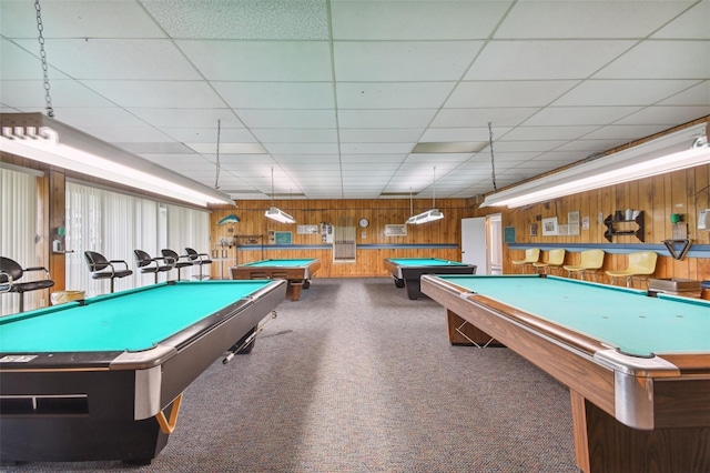 game room featuring a paneled ceiling, wood walls, and dark colored carpet