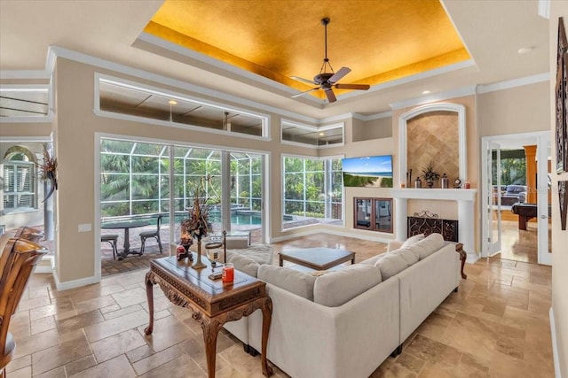 living room featuring a raised ceiling, ceiling fan, crown molding, and a healthy amount of sunlight