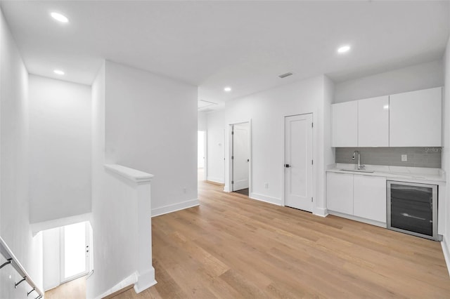 interior space with backsplash, sink, light wood-type flooring, white cabinets, and beverage cooler