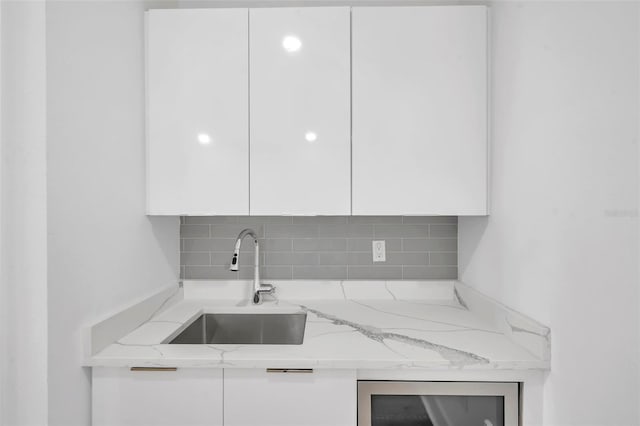 kitchen featuring light stone countertops, beverage cooler, white cabinetry, decorative backsplash, and sink