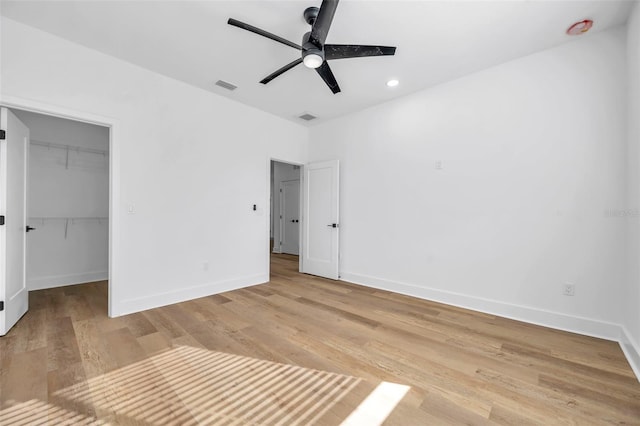 unfurnished bedroom featuring ceiling fan, a walk in closet, a closet, and light wood-type flooring